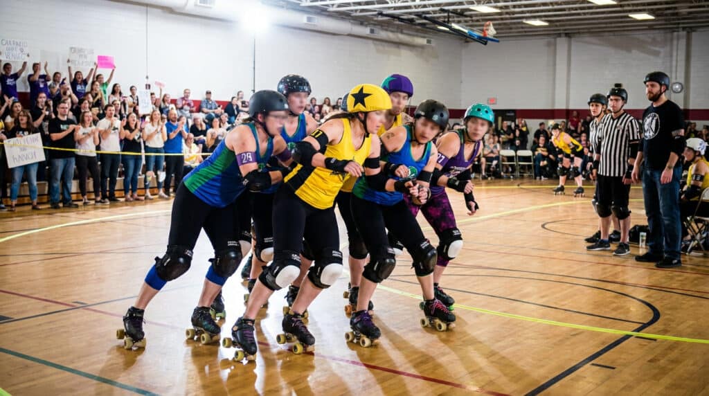 Équipe de roller derby en pleine action lors d’un match avec public et arbitres en arrière plan