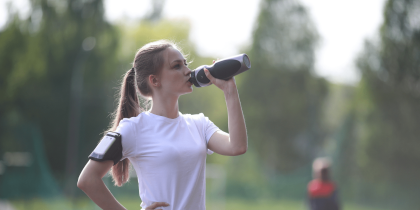 Gourde de sport - femme sportive en t-shirt blanc buvant à une gourde pendant son entraînement en plein air