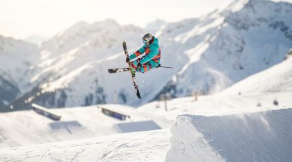 Skieur freestyle réalisant un saut acrobatique dans un snowpark avec un paysage de montagne enneigée
