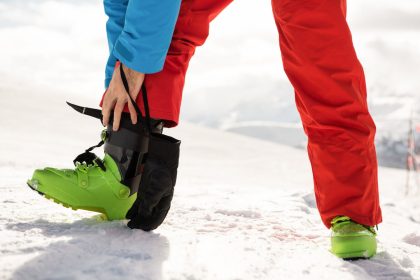 Skieur-ajustant-sa-chaussure-de-ski-verte-sur-une-piste-enneigee-vetu-dun-pantalon-rouge-et-dune-veste-bleue-pour-un-meilleur-confort-et-securite