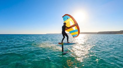 Pratiquant de wing foil glissant au-dessus de l’eau avec une aile gonflable sur une mer calme au soleil
