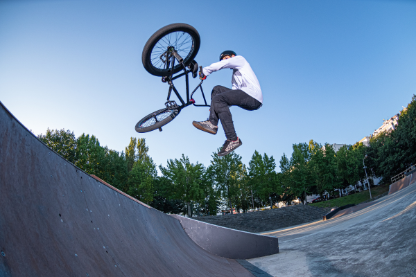Rider effectuant une figure aérienne en BMX freestyle sur une rampe dans un skatepark sous un ciel bleu.