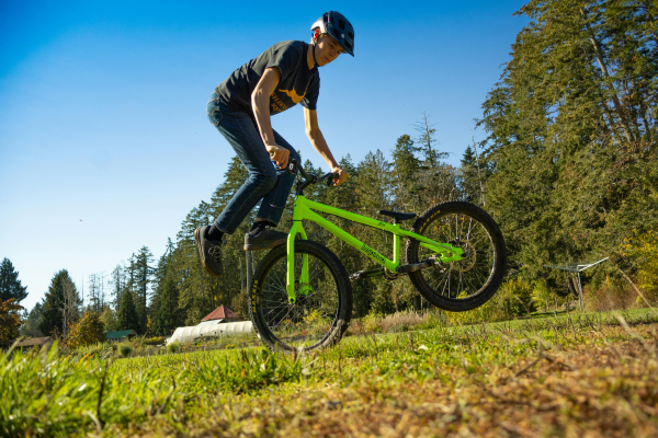 Cycliste réalisant une figure en BMX trial sur un terrain en plein air, entouré d’arbres et de nature.